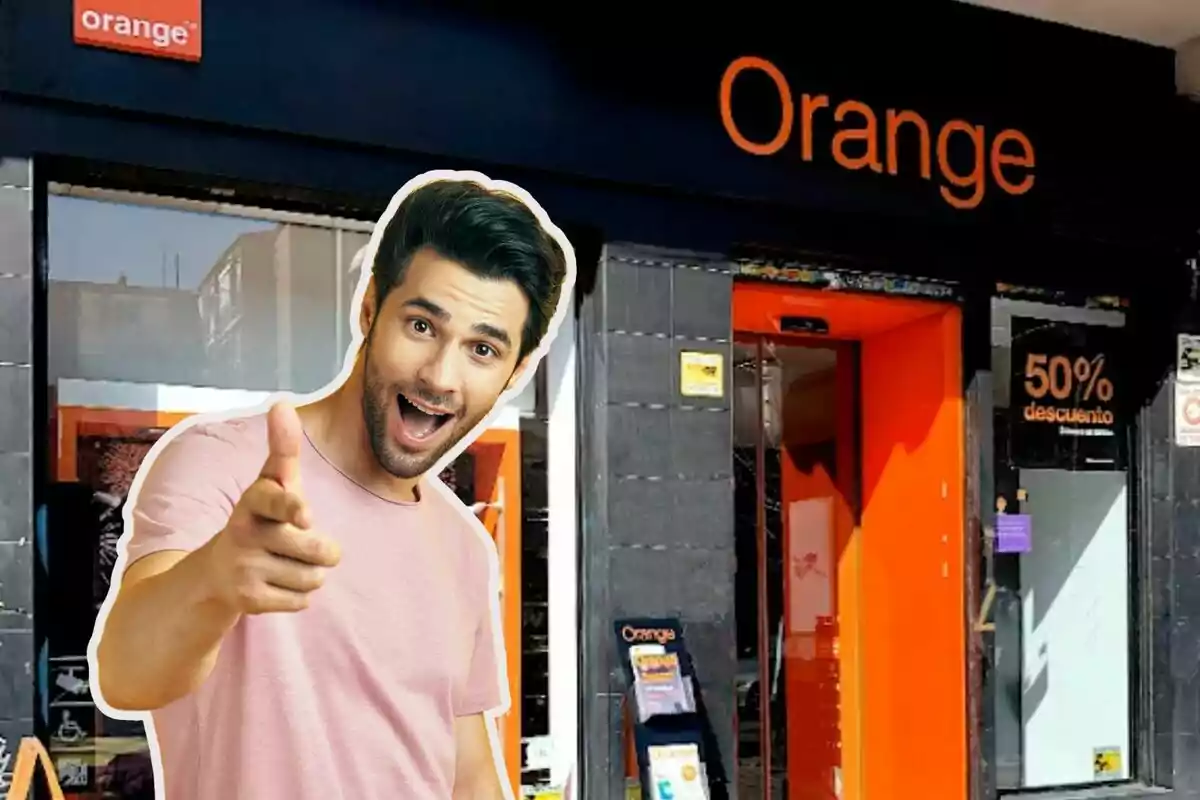 Un hombre sonriente y señalando con el dedo frente a una tienda de Orange con un cartel de descuento del 50%.