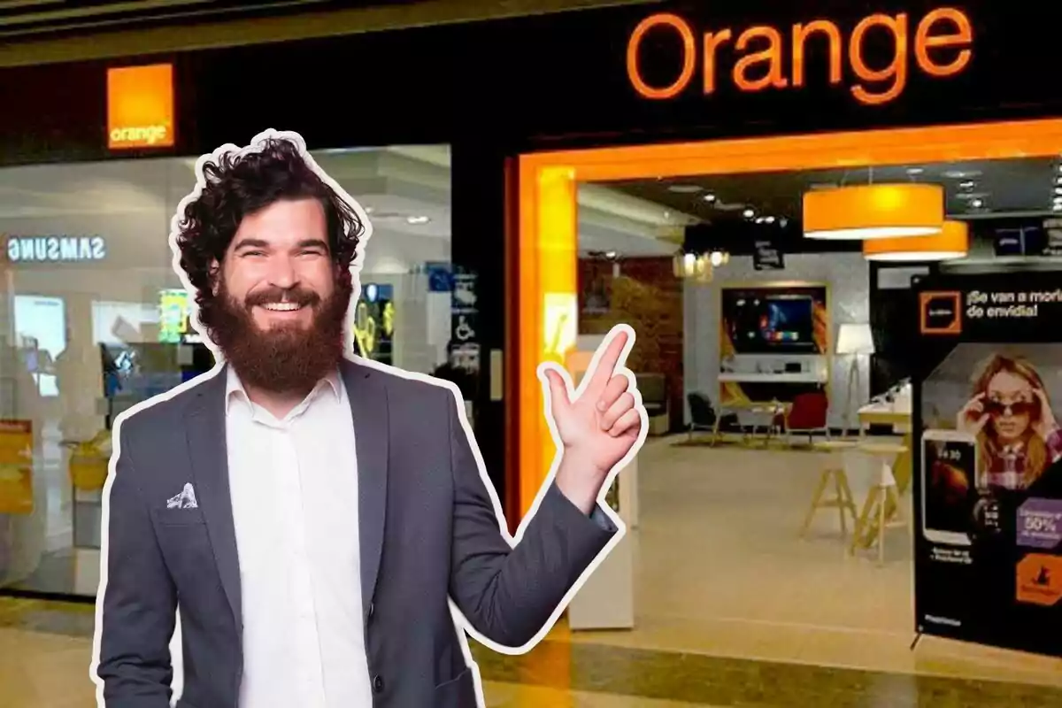 Un hombre sonriente con barba y traje señala hacia una tienda de Orange.