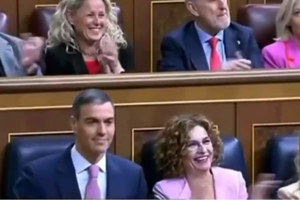 Un grupo de personas sonríe y aplaude en un entorno formal, posiblemente un parlamento o congreso. Un grupo de personas sonríe y aplaude en un entorno formal, posiblemente un parlamento o congreso.
