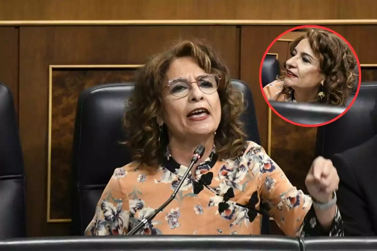 Una mujer con gafas y cabello rizado habla en un micrófono en un entorno formal con un recuadro que muestra un acercamiento de su rostro.