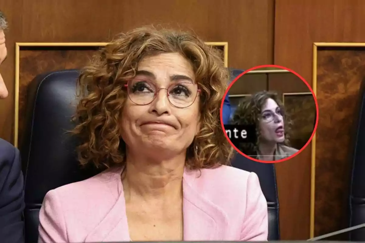 Una persona con expresión pensativa y gafas, vestida con un blazer rosa, está sentada en un entorno formal; hay un recuadro que muestra un primer plano de la misma persona hablando.