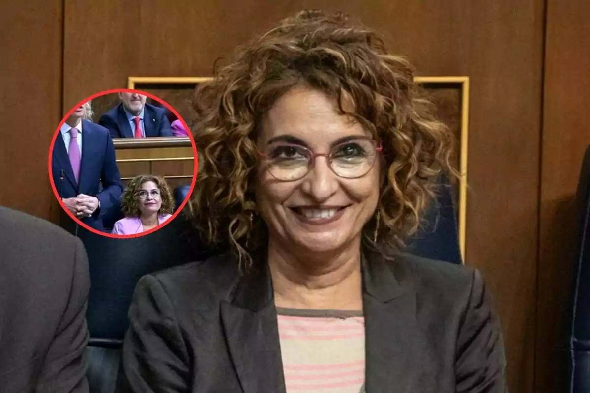 Una mujer con gafas y cabello rizado sonríe mientras está sentada en un entorno formal, con un recuadro que muestra una escena similar en el fondo.
