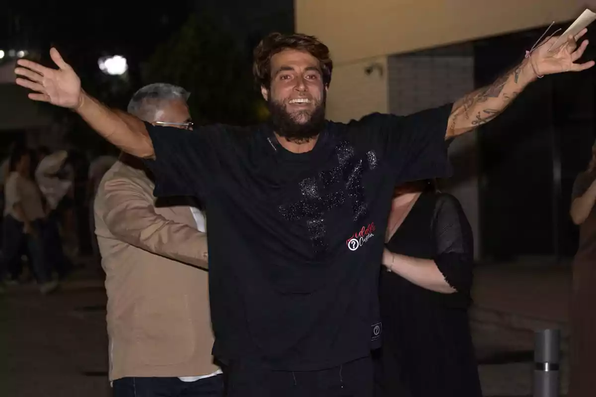 Montoya sonríe con los brazos abiertos en una calle de noche rodeado de otras personas. Montoya sonríe con los brazos abiertos en una calle de noche rodeado de otras personas.