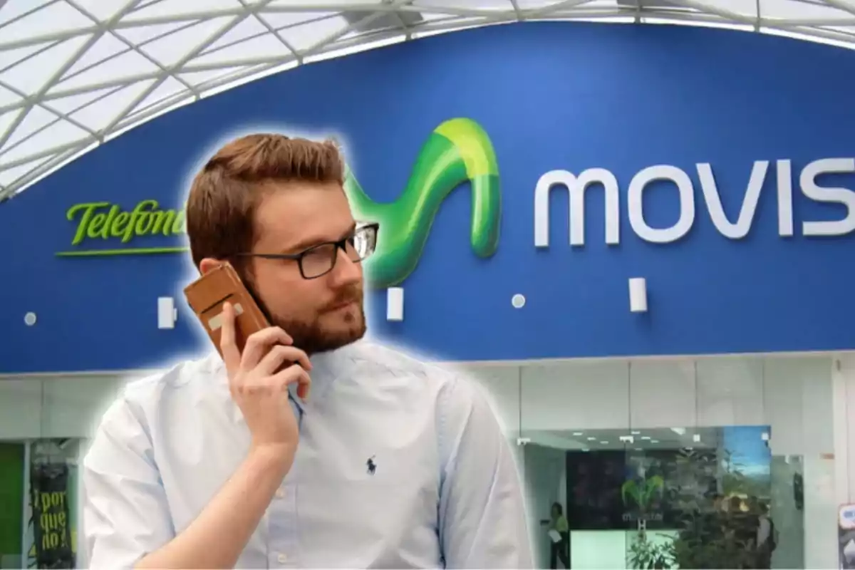 Un hombre con gafas y barba está hablando por teléfono frente a una tienda de Movistar.