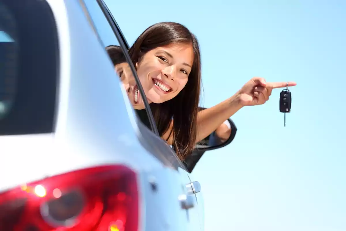 Mujer sonriente asomada por la ventana de un coche sosteniendo una llave de auto.