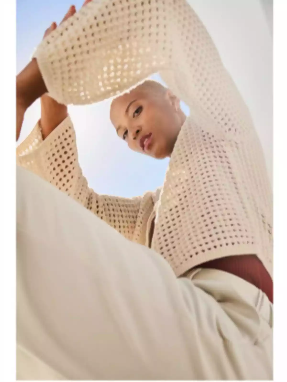 Persona con suéter de punto claro y pantalones beige, vista desde un ángulo bajo con el cielo azul de fondo. Persona con suéter de punto claro y pantalones beige, vista desde un ángulo bajo con el cielo azul de fondo.