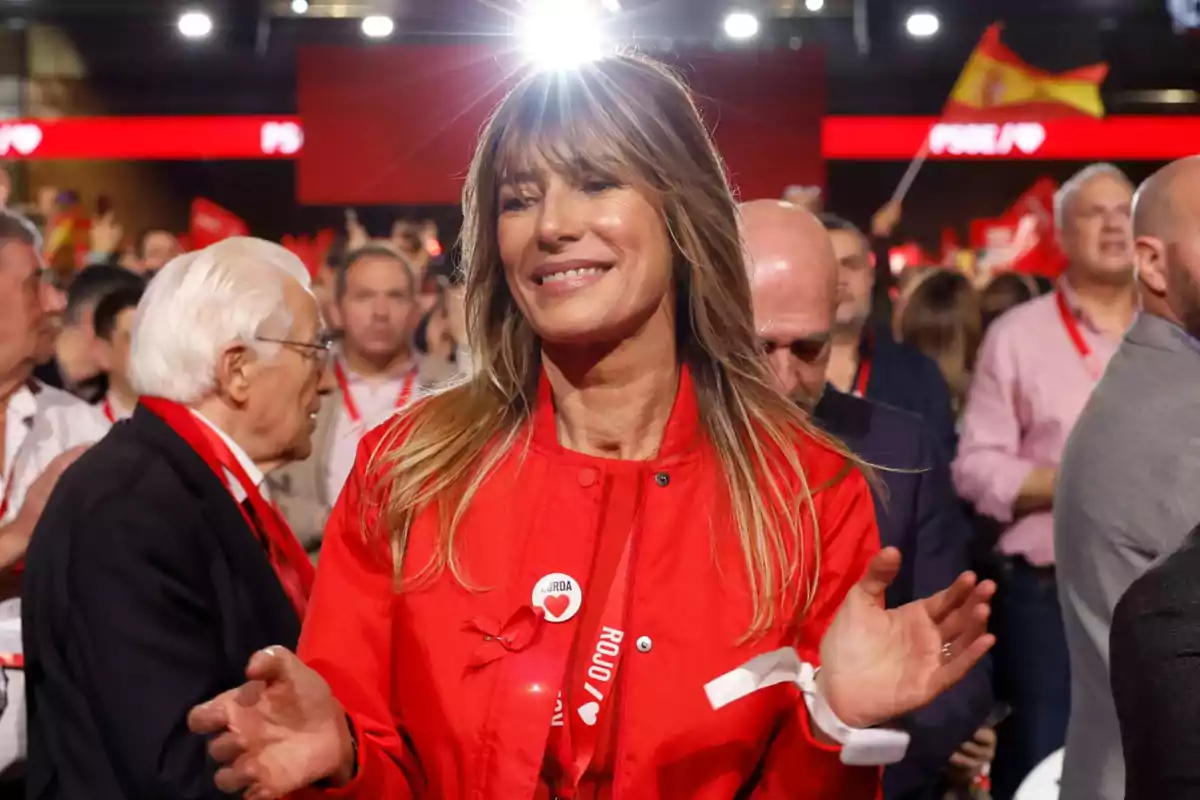 Una mujer sonriente con chaqueta roja en un evento rodeada de personas. Una mujer sonriente con chaqueta roja en un evento rodeada de personas.