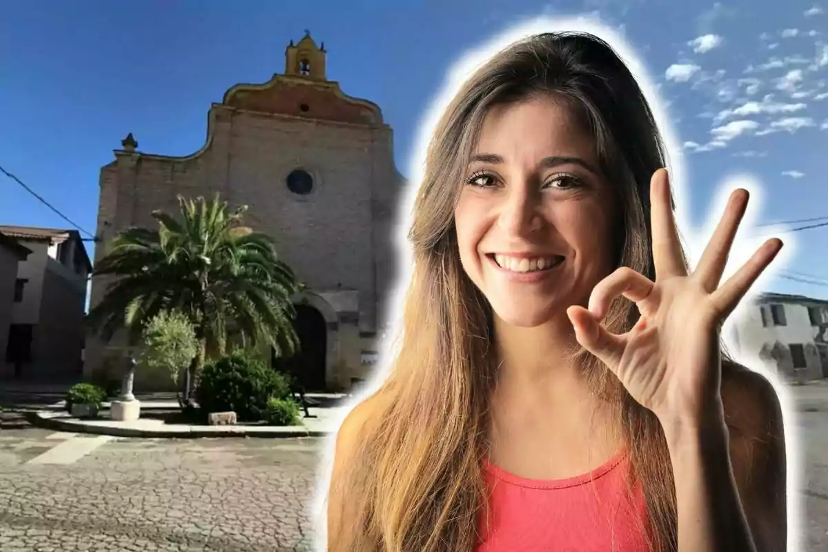 Mujer sonriendo y haciendo el gesto de "OK" con la mano frente a una iglesia con una palmera en la plaza.