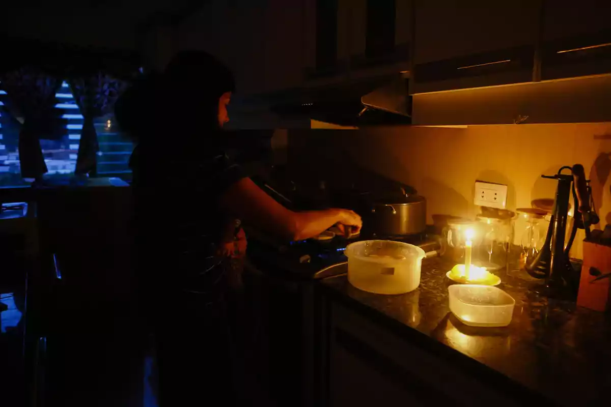 Una persona cocina en una cocina oscura iluminada por una vela sobre la encimera.