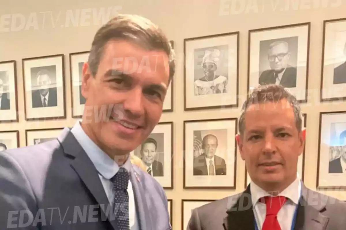 Dos personas posan para una foto frente a una pared con retratos enmarcados.