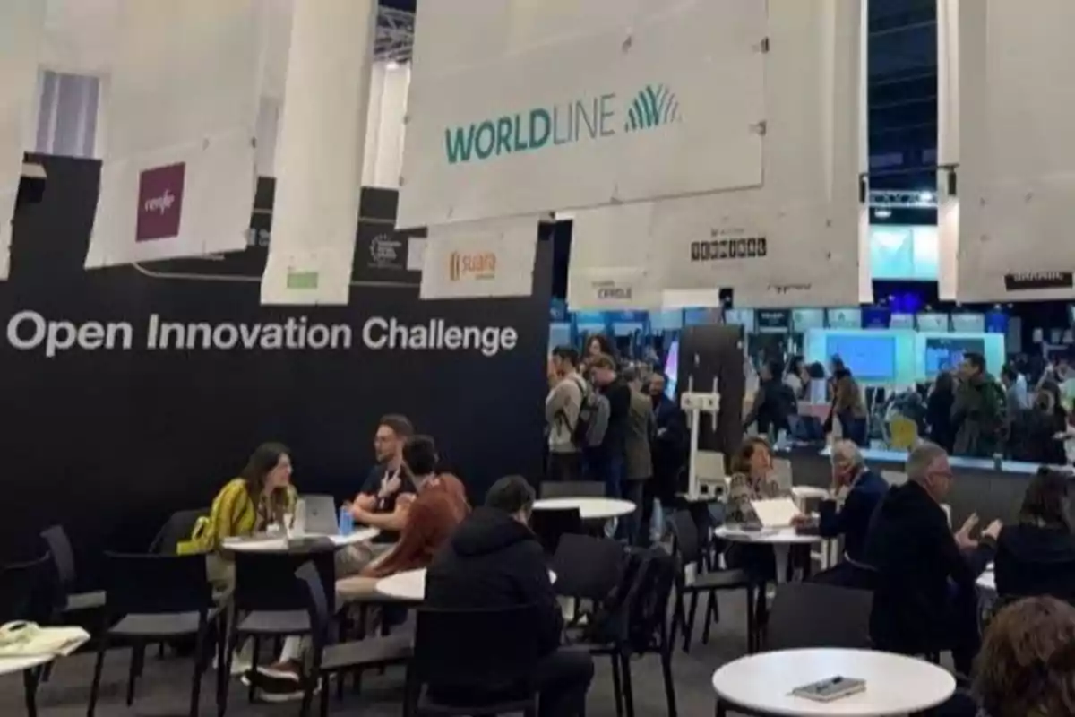 People seated at round tables at an innovation event with hanging signs and a bustling atmosphere.