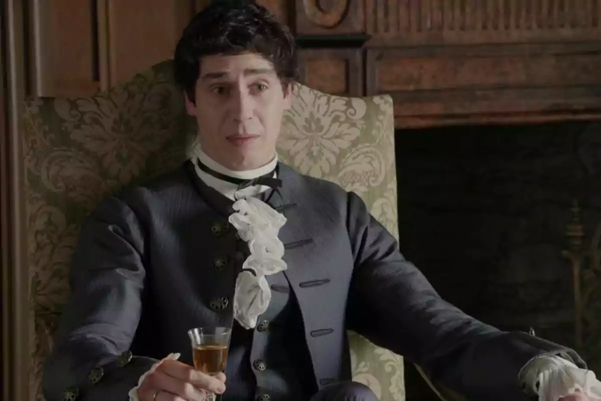 Nacho Olaizola vestido con ropa de época, sentado en una silla elegante, sosteniendo una copa en Valle Salvaje. Nacho Olaizola vestido con ropa de época, sentado en una silla elegante, sosteniendo una copa en Valle Salvaje.