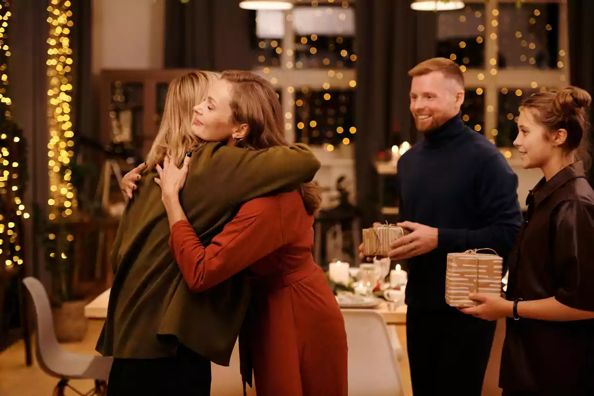 Un grupo de personas intercambia abrazos y regalos en una reunión festiva con luces brillantes de fondo.