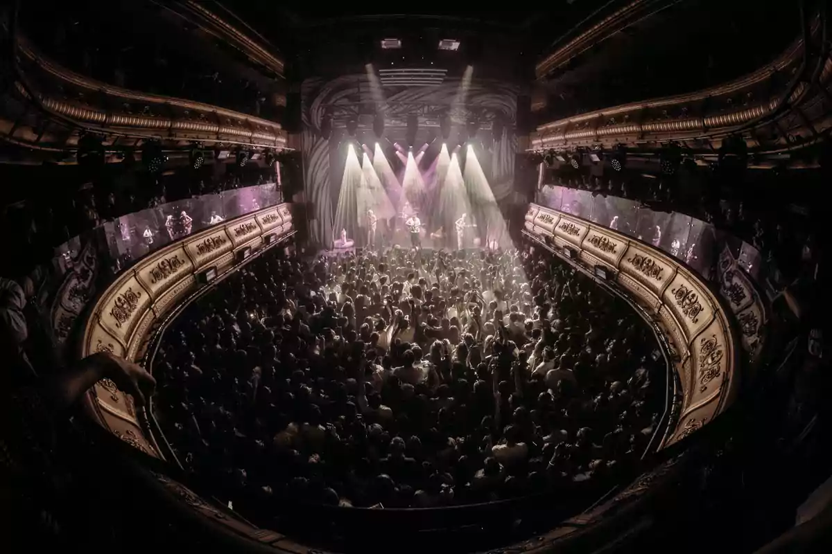 A crowd enjoys a concert in a theater with dramatic lighting and elegant decor.