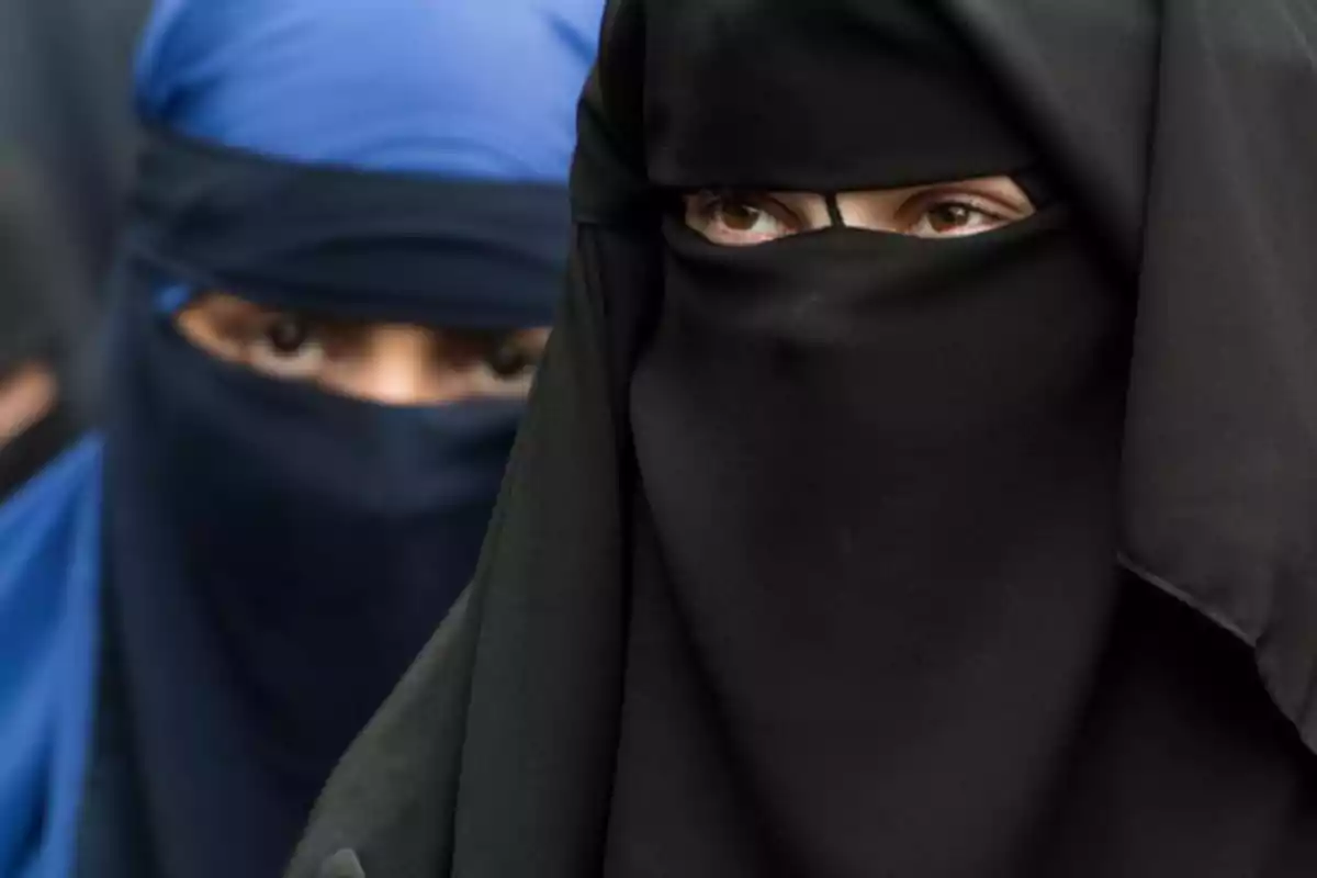 Dos mujeres con velo islámico, una con niqab negro en primer plano y otra con hiyab azul en el fondo, mostrando solo sus ojos. Dos mujeres con velo islámico, una con niqab negro en primer plano y otra con hiyab azul en el fondo, mostrando solo sus ojos.
