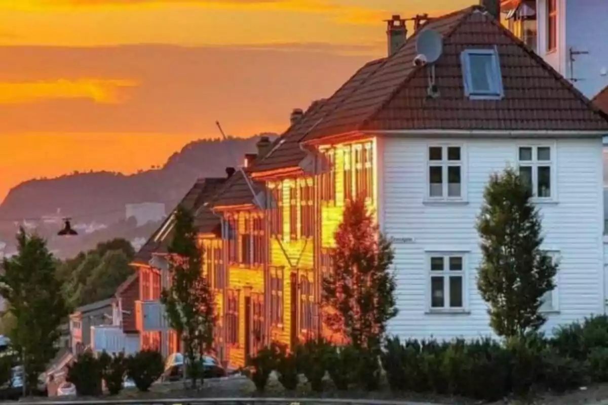 Casas blancas con techos de tejas rojas iluminadas por el sol al atardecer, con un cielo anaranjado y montañas al fondo.