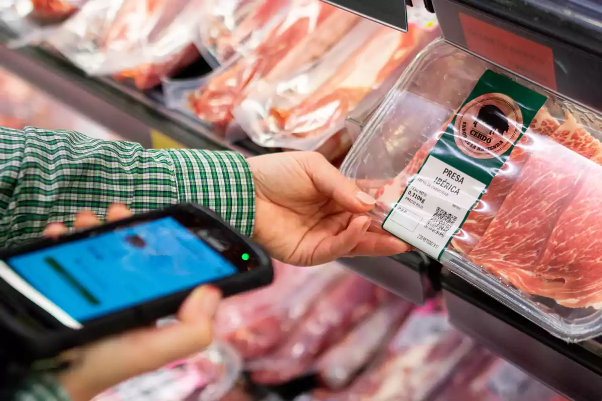 A person holds a package of meat labeled "Presa Ibérica" while using a mobile device in a store.