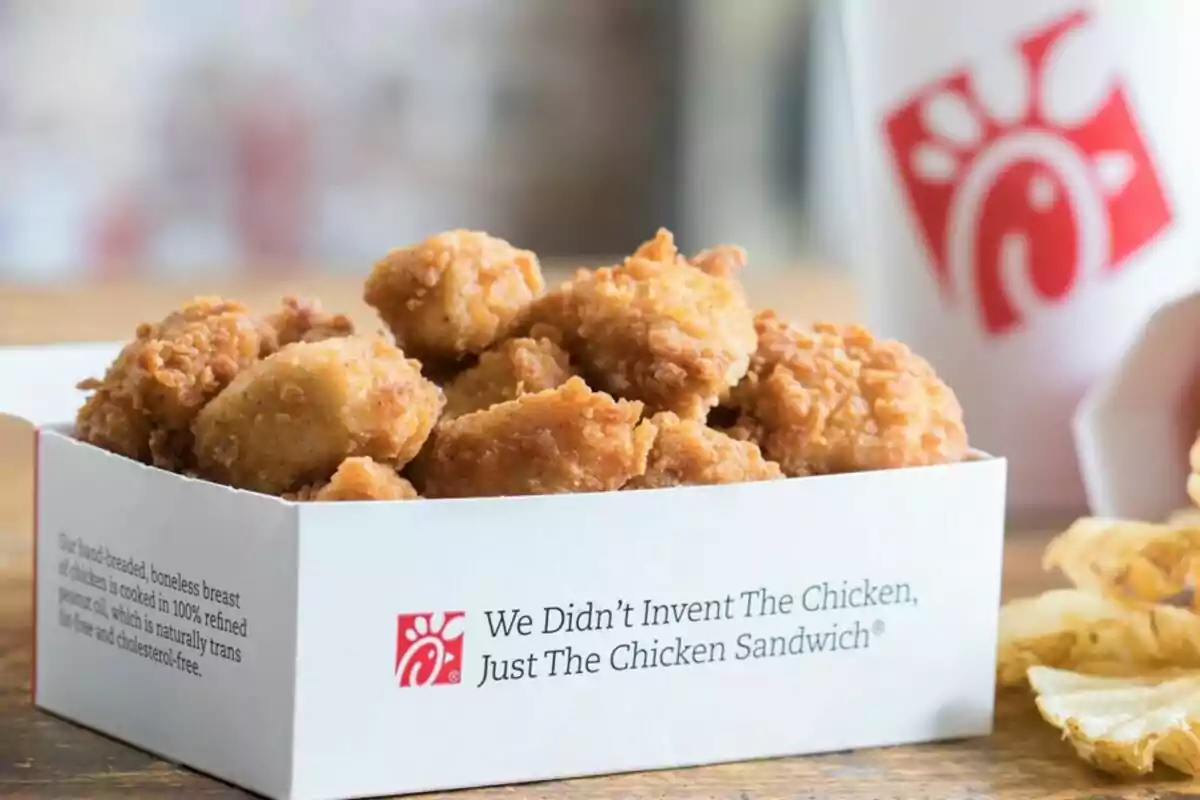 A box of crispy chicken nuggets next to a cup with the Chick-Fil-A logo. A box of crispy chicken nuggets next to a cup with the Chick-Fil-A logo.