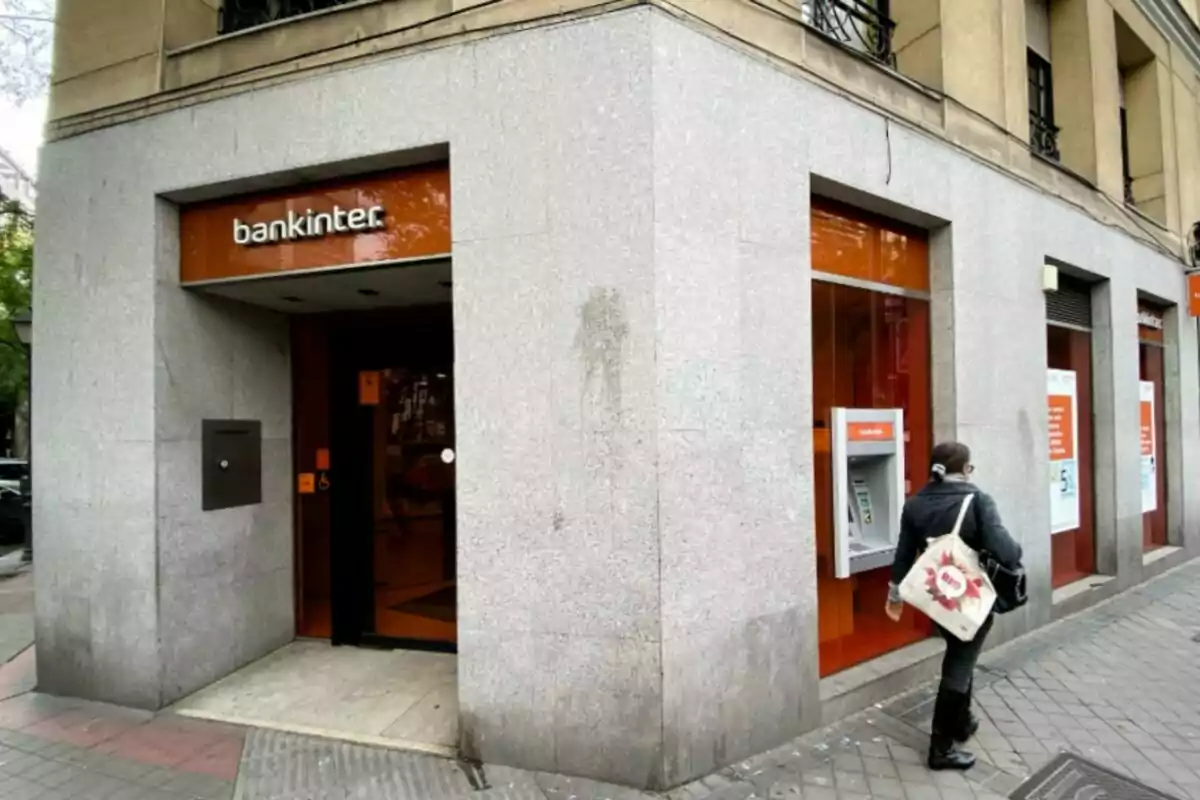Oficina de Bankinter con una señora de espaldas con abrigo negro y una bolsa blanca