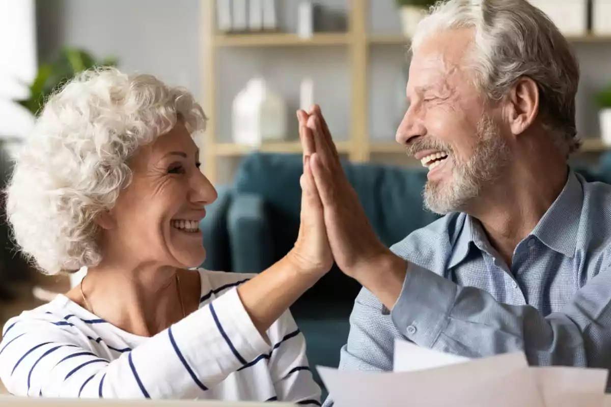 Una pareja de personas mayores sonriendo y chocando las manos en un ambiente hogareño.