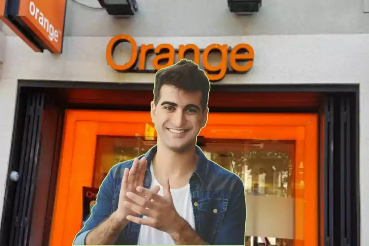 A smiling man in a denim shirt stands in front of an Orange store.