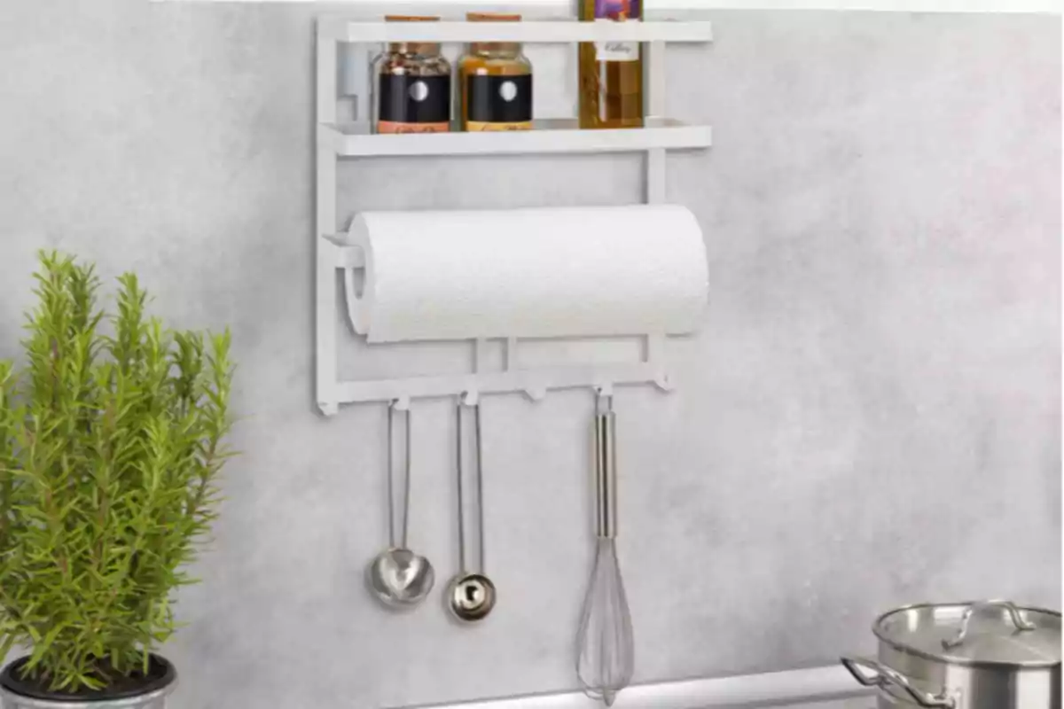 Organizador de cocina blanco montado en la pared con especias, un rollo de papel, utensilios colgando y una planta al lado Organizador de cocina blanco montado en la pared con especias, un rollo de papel, utensilios colgando y una planta al lado