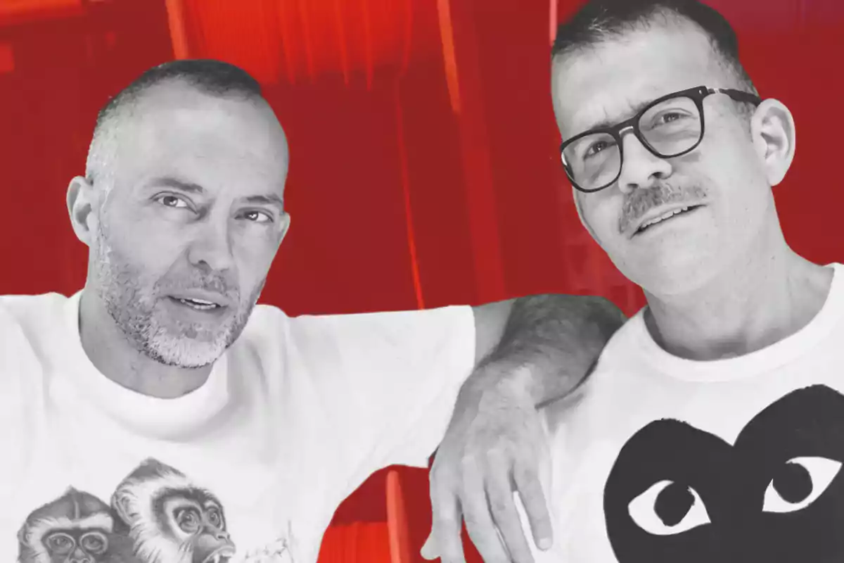 Dos personas posando juntas con camisetas blancas y un fondo rojo.