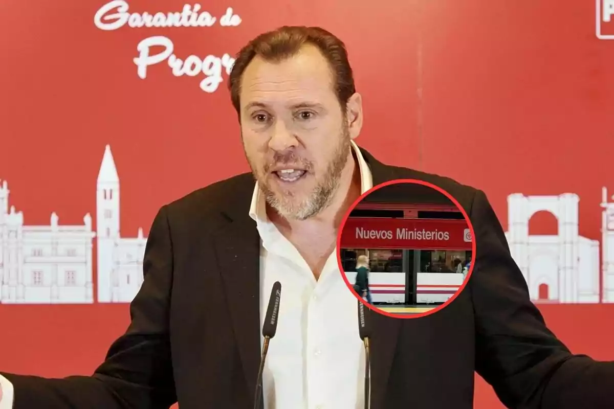 Un hombre con barba y cabello castaño está hablando frente a un micrófono con un fondo rojo que tiene texto blanco y un diseño de edificios; hay un círculo que muestra una estación de tren llamada "Nuevos Ministerios".