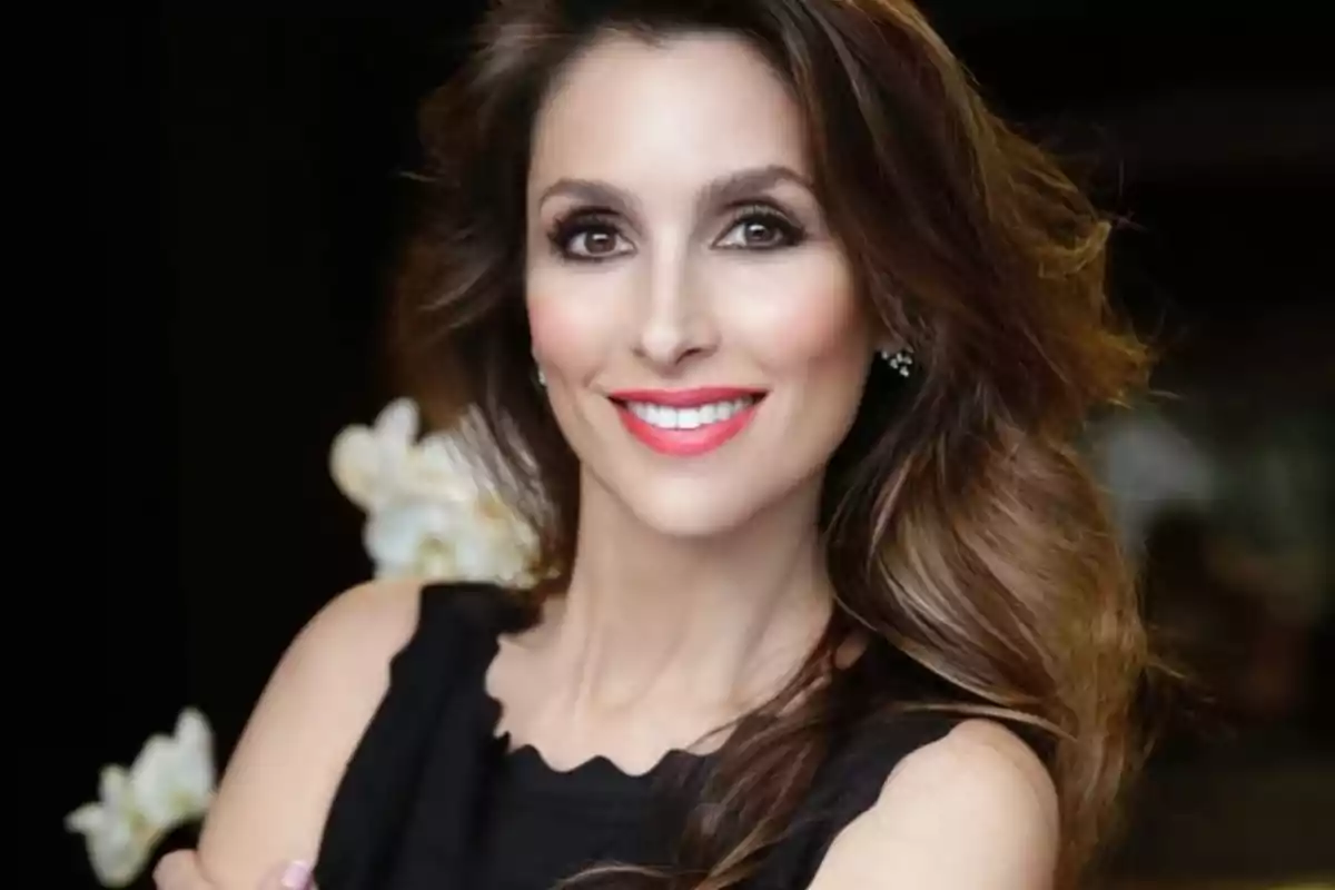 Una mujer sonriente con cabello largo y ondulado y un vestido negro. Una mujer sonriente con cabello largo y ondulado y un vestido negro.