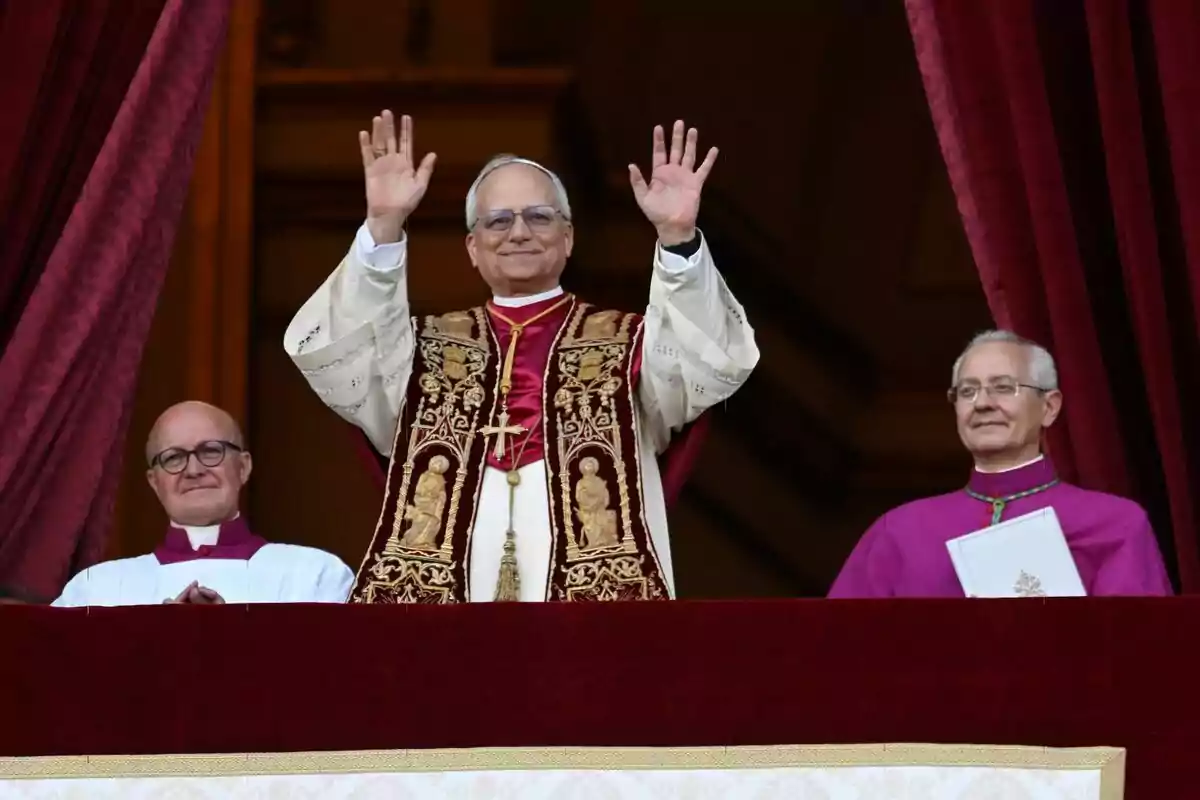 Pope Leo XIV dressed in religious garments raises his hands from a balcony accompanied by two other people. Pope Leo XIV dressed in religious garments raises his hands from a balcony accompanied by two other people.