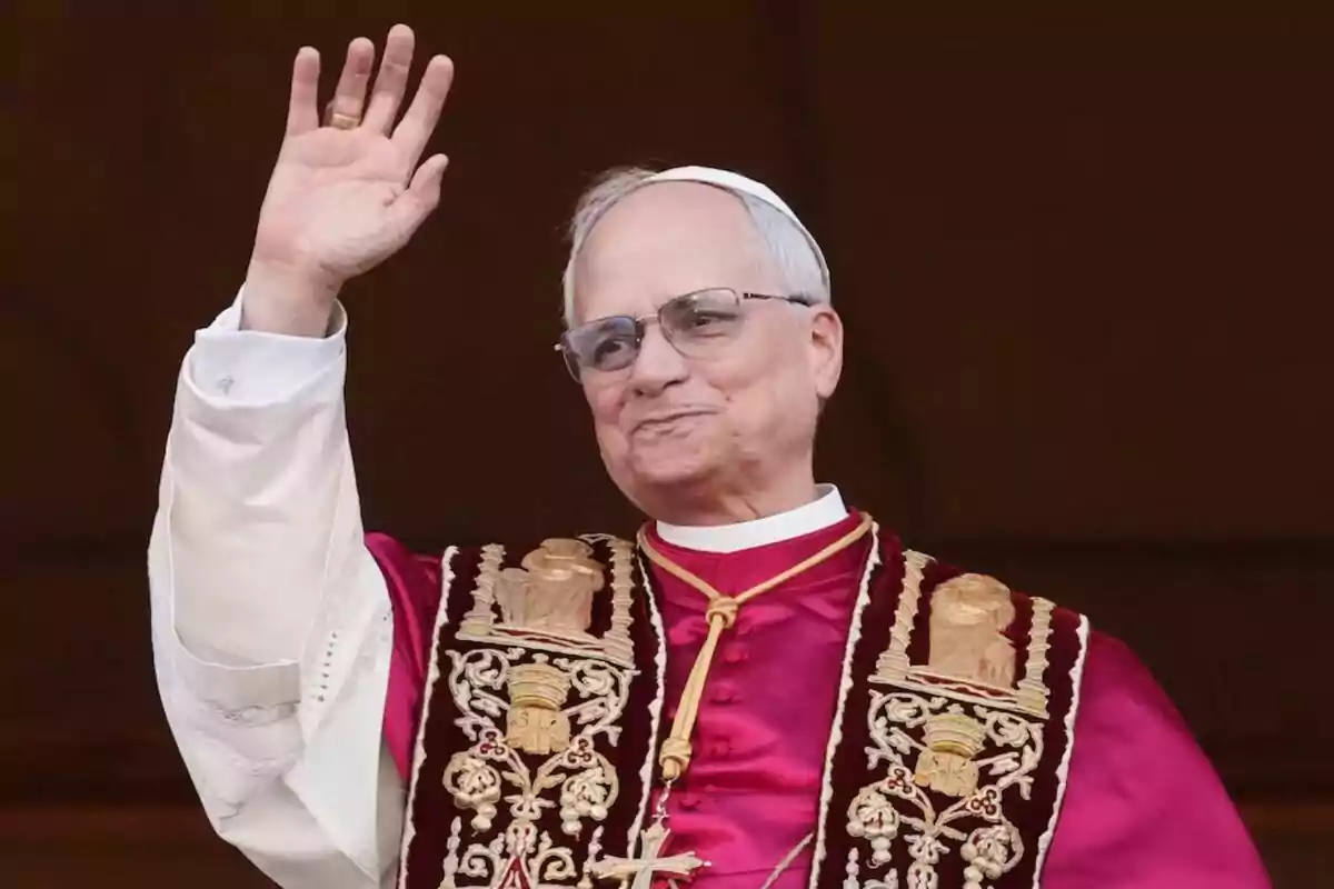 An elderly man with glasses and religious attire raises his hand in greeting. An elderly man with glasses and religious attire raises his hand in greeting.