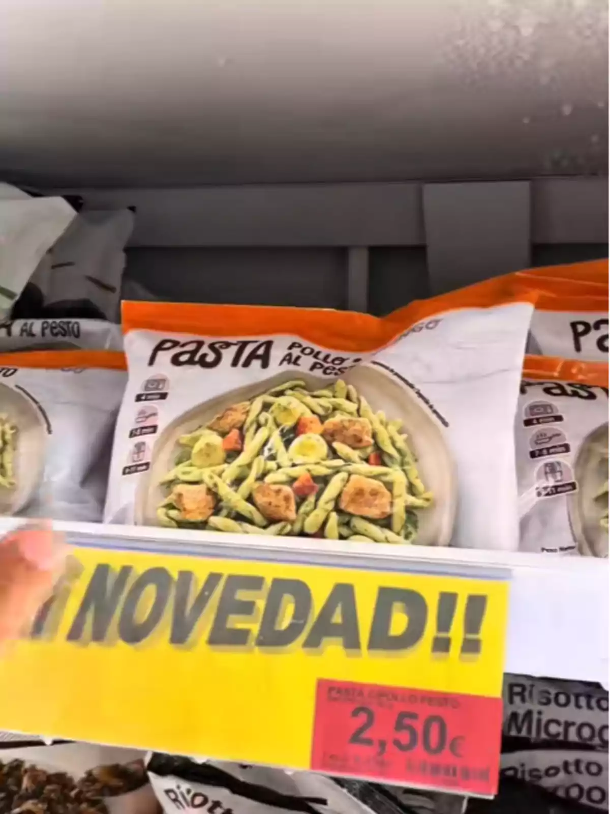 Paquete de pasta con pollo al pesto en un estante de supermercado con un cartel amarillo que dice Paquete de pasta con pollo al pesto en un estante de supermercado con un cartel amarillo que dice