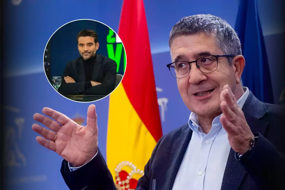 Un hombre de cabello canoso y gafas habla gesticulando con las manos frente a una bandera de España mientras en la esquina superior izquierda aparece un recuadro con otro hombre de barba y cabello oscuro sentado con los brazos cruzados.