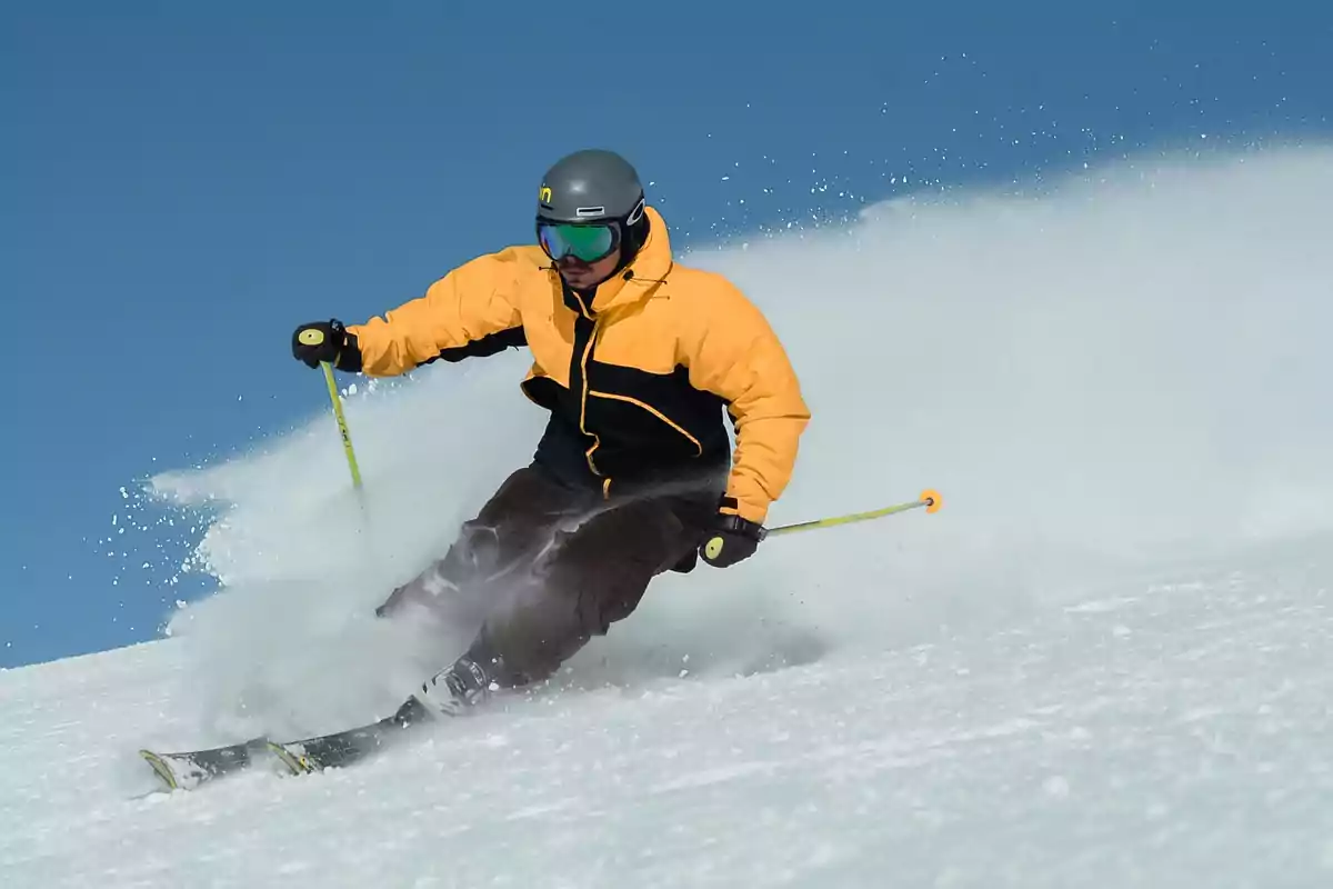 Person skiing in the snow with a yellow jacket and a gray helmet.