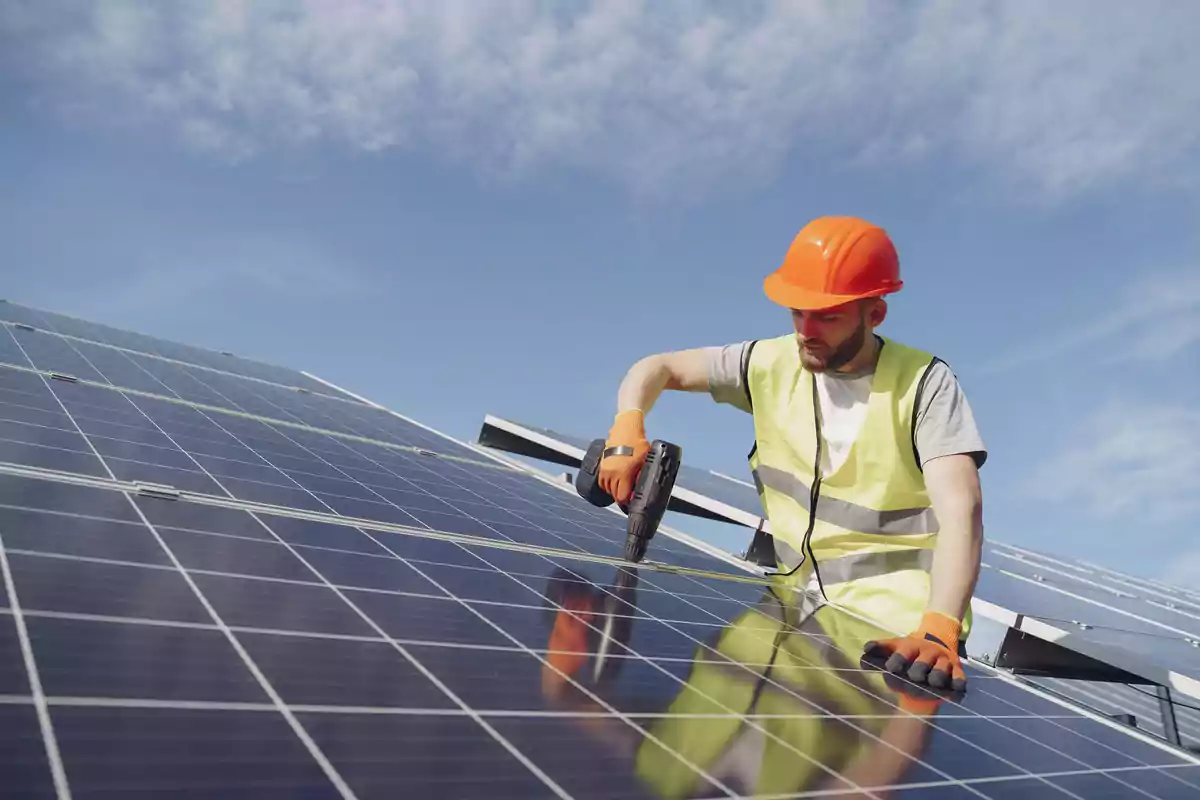 Man with a helmet and safety vest installing solar panels under a clear sky.