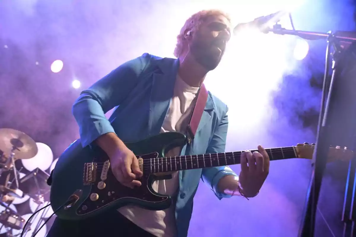 Músico tocando la guitarra eléctrica en un escenario con luces y humo.