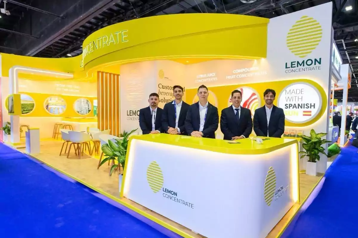 Un grupo de personas en un stand de exhibición de Lemon Concentrate con un diseño moderno y colores amarillos y blancos.