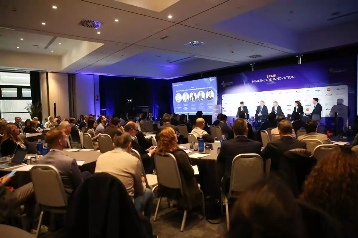 Personas asistiendo a una conferencia sobre innovación en salud en un salón de eventos.