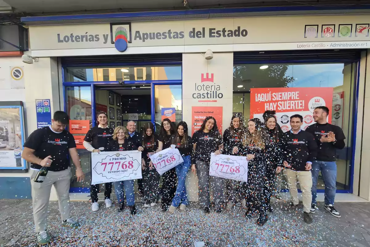 Un grupo de personas celebra frente a una administración de lotería con carteles del número ganador y confeti en el aire.