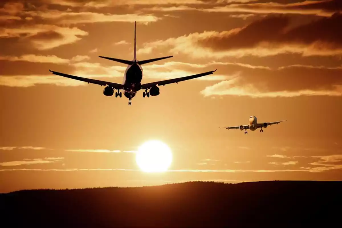 Dos aviones volando hacia el horizonte con un atardecer dorado de fondo.