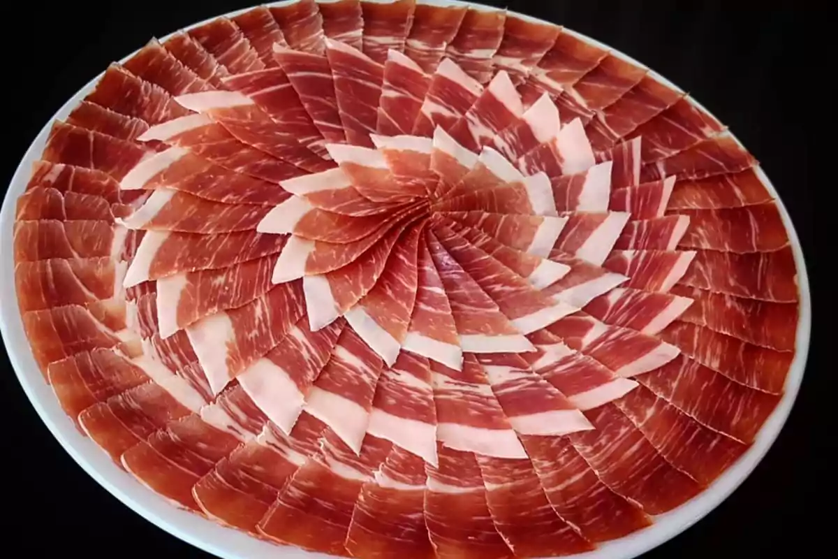 Un plato de jamón ibérico finamente cortado y dispuesto en un patrón circular.