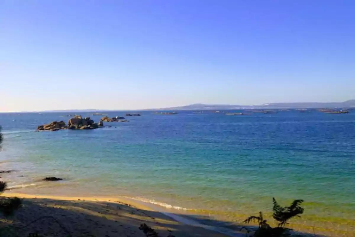 Playa con arena dorada y agua azul clara, con rocas en el mar y un cielo despejado.