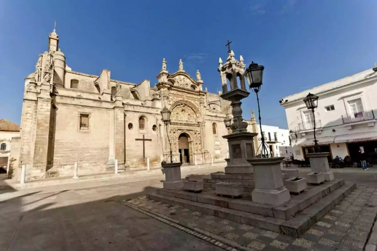 Iglesia histórica con fachada detallada y plaza con faroles y cruz en primer plano bajo un cielo despejado. Iglesia histórica con fachada detallada y plaza con faroles y cruz en primer plano bajo un cielo despejado.