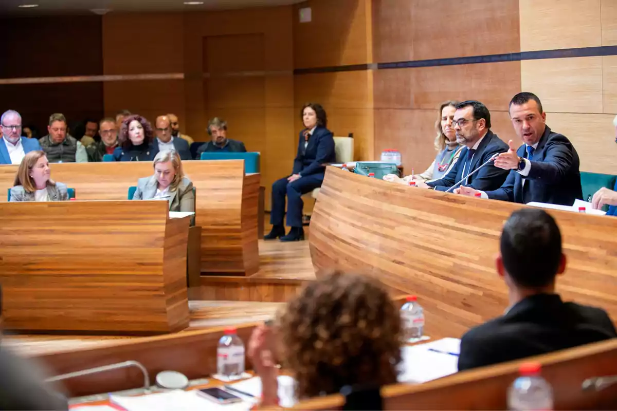 People gathered in a wood-paneled conference room, some taking notes and others participating in the discussion.