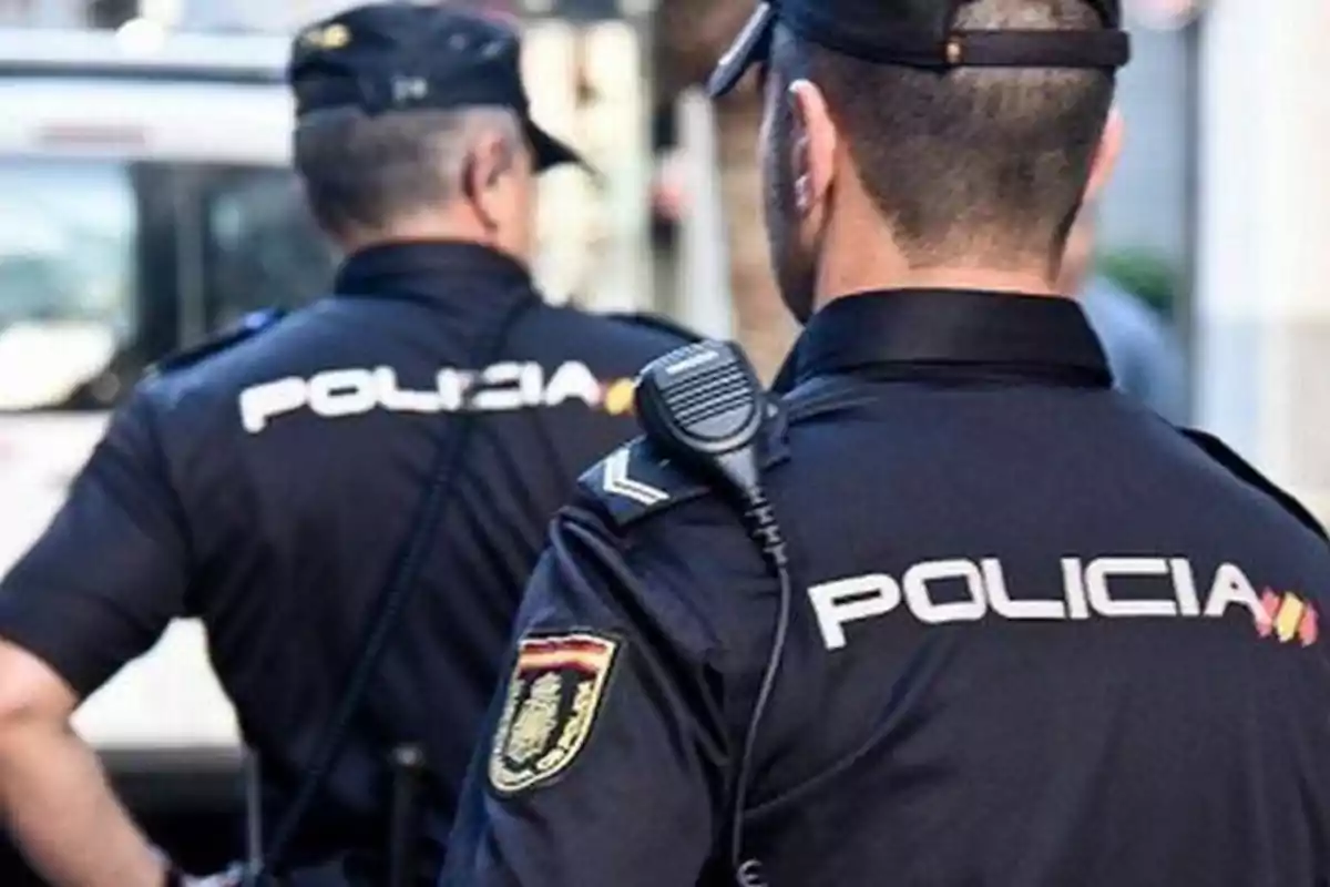 Dos policías de espaldas con uniformes oscuros y la palabra Dos policías de espaldas con uniformes oscuros y la palabra