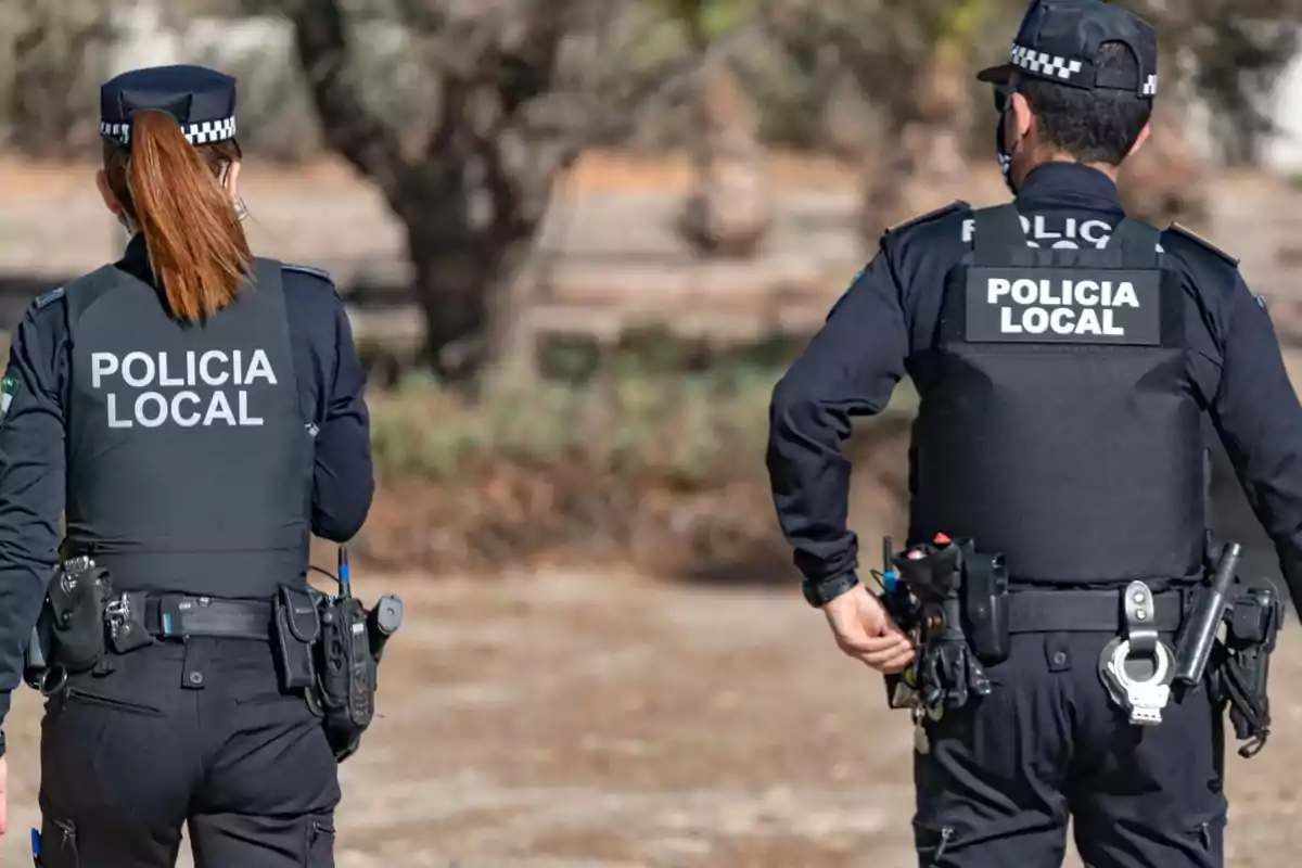 Dos agentes de la policía local caminando de espaldas en un entorno al aire libre. Dos agentes de la policía local caminando de espaldas en un entorno al aire libre.