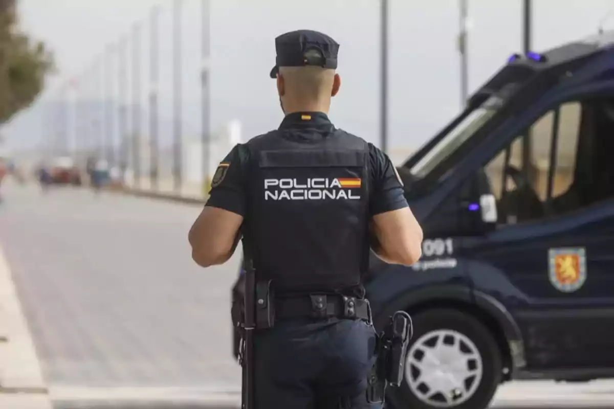 Agente de la Policía Nacional de España de espaldas junto a una patrulla en la vía pública