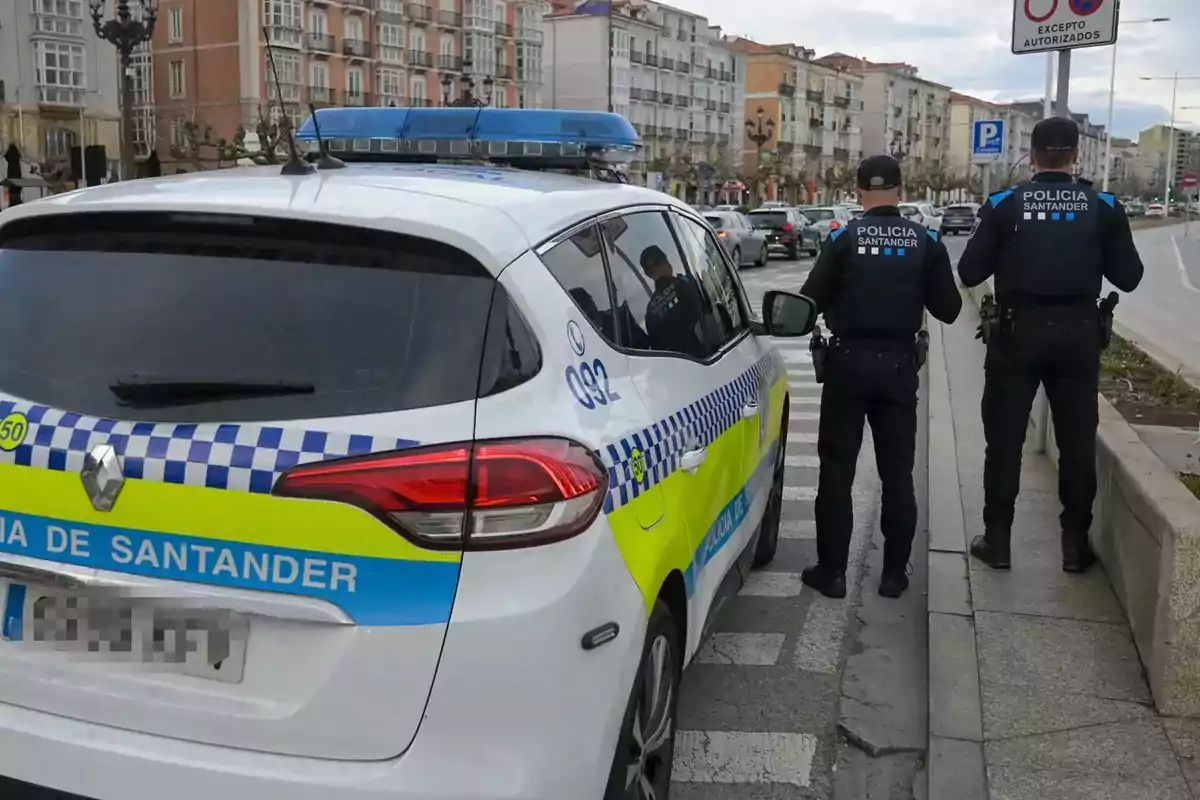 Un coche de policía de Santander estacionado en una calle con dos agentes de pie junto a él.