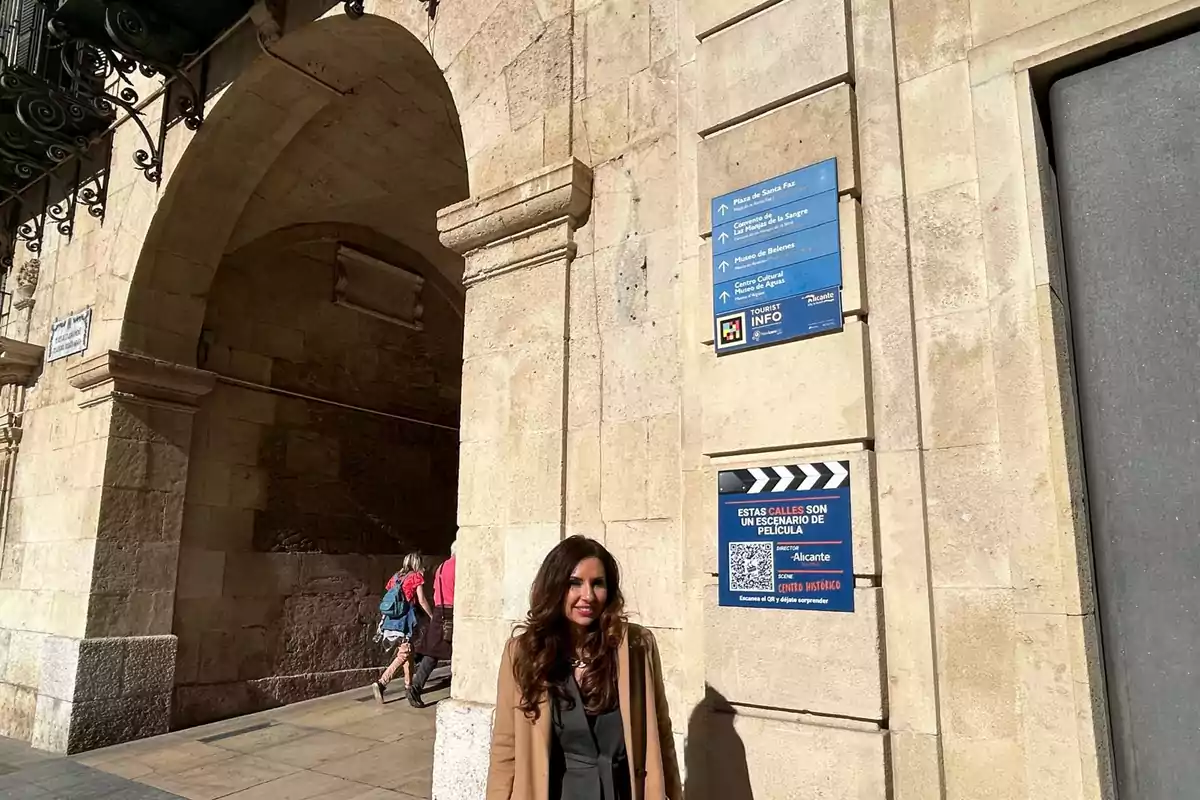 A person standing next to a stone building with arches and tourist signs on the wall.