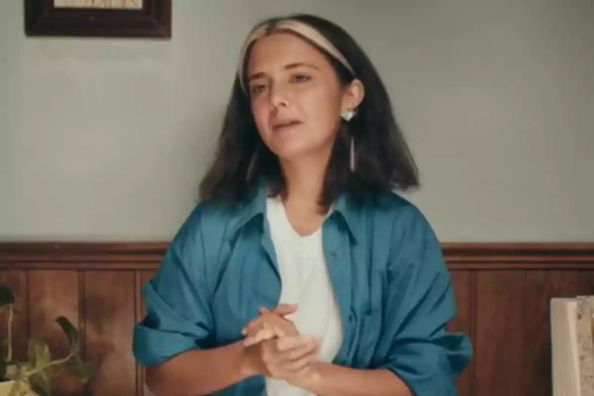 Alejandra Armero, lleva una camisa azul sobre una camiseta blanca y está en una habitación con paredes de madera y una planta a su lado. Alejandra Armero, lleva una camisa azul sobre una camiseta blanca y está en una habitación con paredes de madera y una planta a su lado.